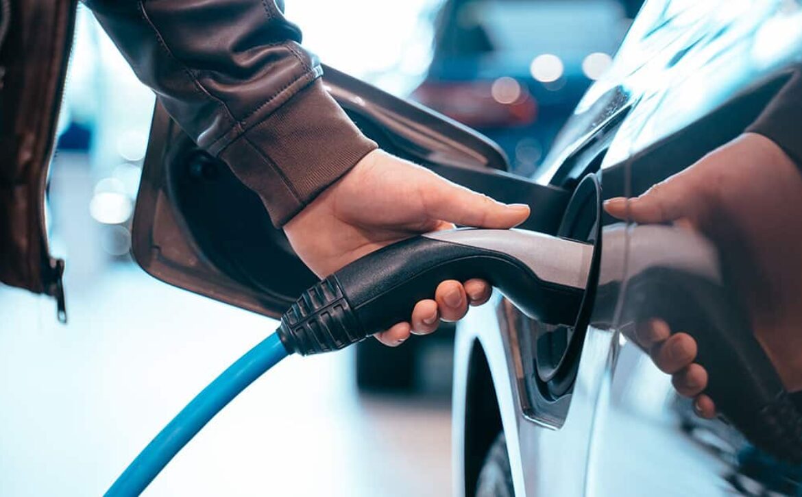 Human hand is holding Electric Car Charging connect to Electric car